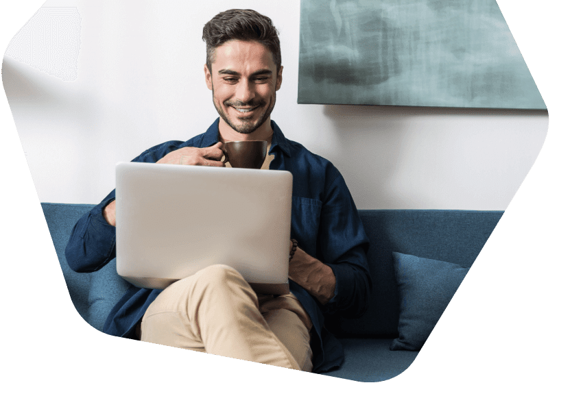 Man on sofa drinking coffee whilst using his laptop