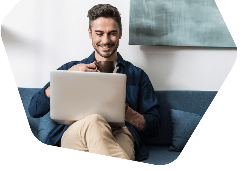 Man on sofa drinking coffee whilst using his laptop
